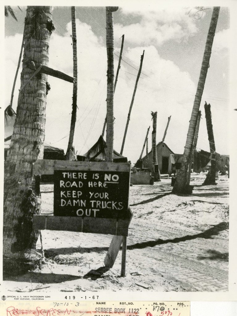 Sarcastic sign made by Seabees on Gilbert Island. Sign reads, "there is NO road here keep your damn trucks out".